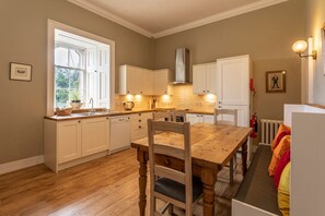 A kitchen with wooden cabinets, a dining table, and a window with a view of greenery. - Esk Tower - Five Bedroom Apartment, Sleeps 10 (Brechin)