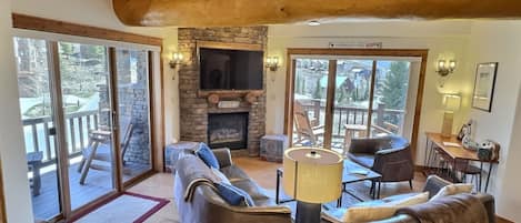 A cozy living room with a stone fireplace, leather sofas, and a large TV.