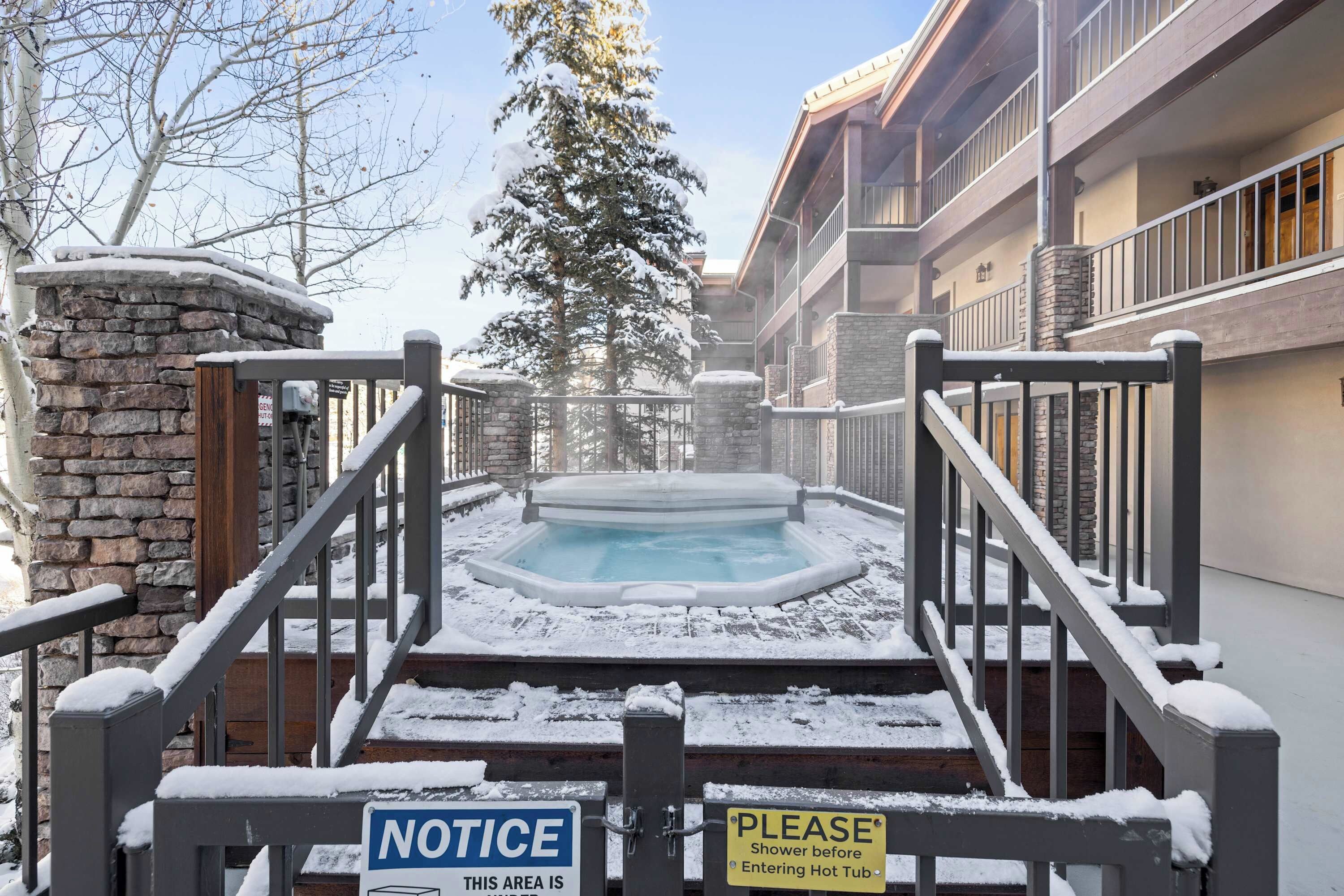 Un espace extérieur enneigé comprenant un jacuzzi, des murs en pierre et un escalier en bois.