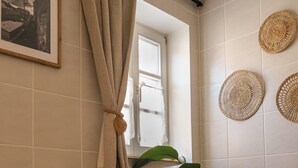 A bathroom with a window, a framed picture, a potted plant, and woven wall decor.