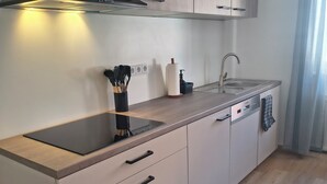 A modern kitchen with a black induction cooktop, a stainless steel sink, and wooden cabinets.