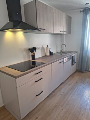 Een moderne keuken met een zwart inductiefornuis, een roestvrijstalen spoelbak en houten keukenkastjes.