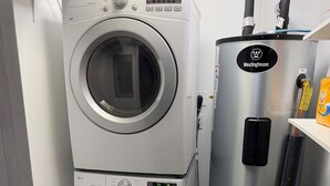 Une buanderie équipée de deux machines à laver LG à chargement frontal, superposées, et d’un chauffe-eau Westinghouse.