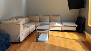 Un salon moderne avec un canapé d’angle, une petite table basse, un téléviseur à écran plat fixé au mur et un plancher en bois.