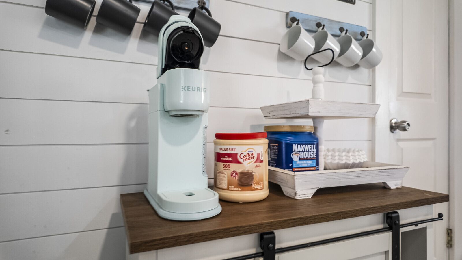 Cuina amb una màquina de cafè Keurig, un envasament de crema de cafè i un recipient de cafè Maxwell House.