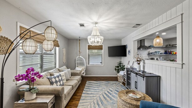 A modern living room with a sofa, a coffee table, a hanging chair, a TV, and a kitchen area with cabinets and a counter.