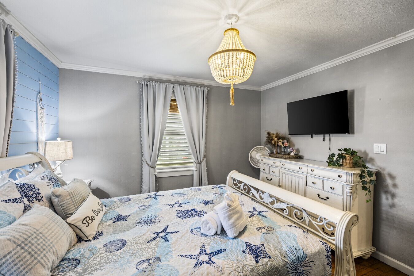A bedroom with a bed, a dresser, a television, and a chandelier.
