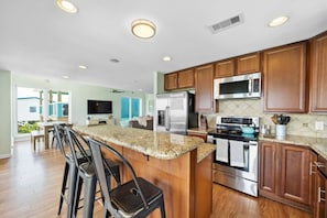 A kitchen with wooden cabinets, a granite countertop, stainless steel appliances, and a bar area with stools. - Waterfront Bay Home with Pool & Private Pier (Kemah Area)
