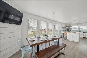 A modern kitchen with a dining area, large windows, and a view of the outside.