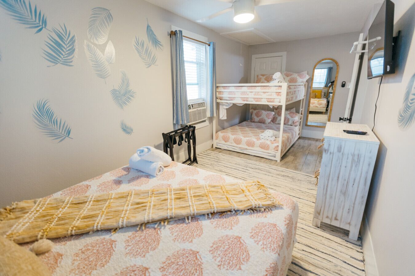 A room with two bunk beds, a small desk, a mirror, and a window with curtains.