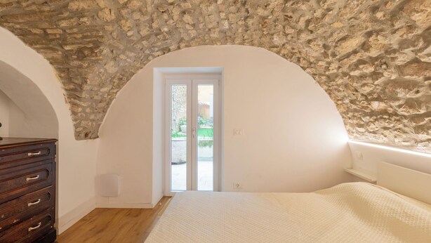 Een slaapkamer met een stenen plafond, een houten dressoir, een bed en een deur naar buiten.