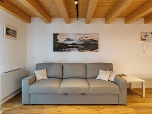 Un sofá gris con cojines estampados, una mesa blanca y un cuadro de un paisaje en la pared.