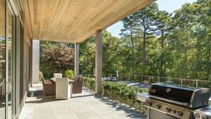 Patio esterno con barbecue, area salotto e vista sugli alberi.