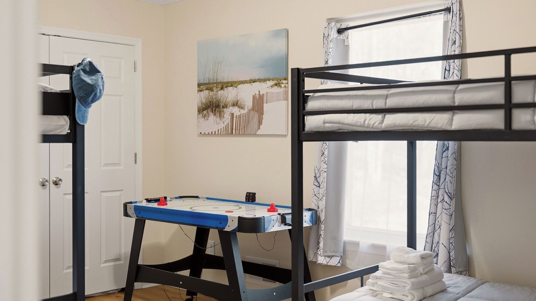 A room with bunk beds, a foosball table, a door, a window with curtains, and a painting on the wall.