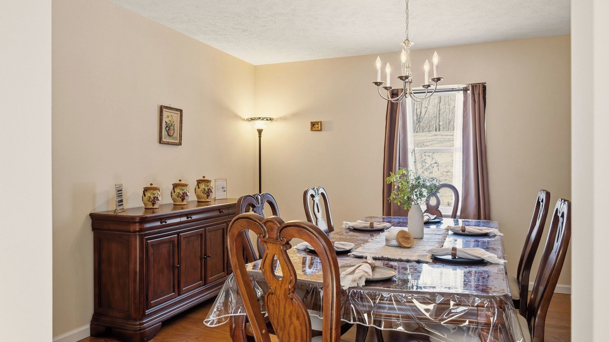 A dining area with a table set for four, wooden chairs, a chandelier, and a cabinet with decorative items.