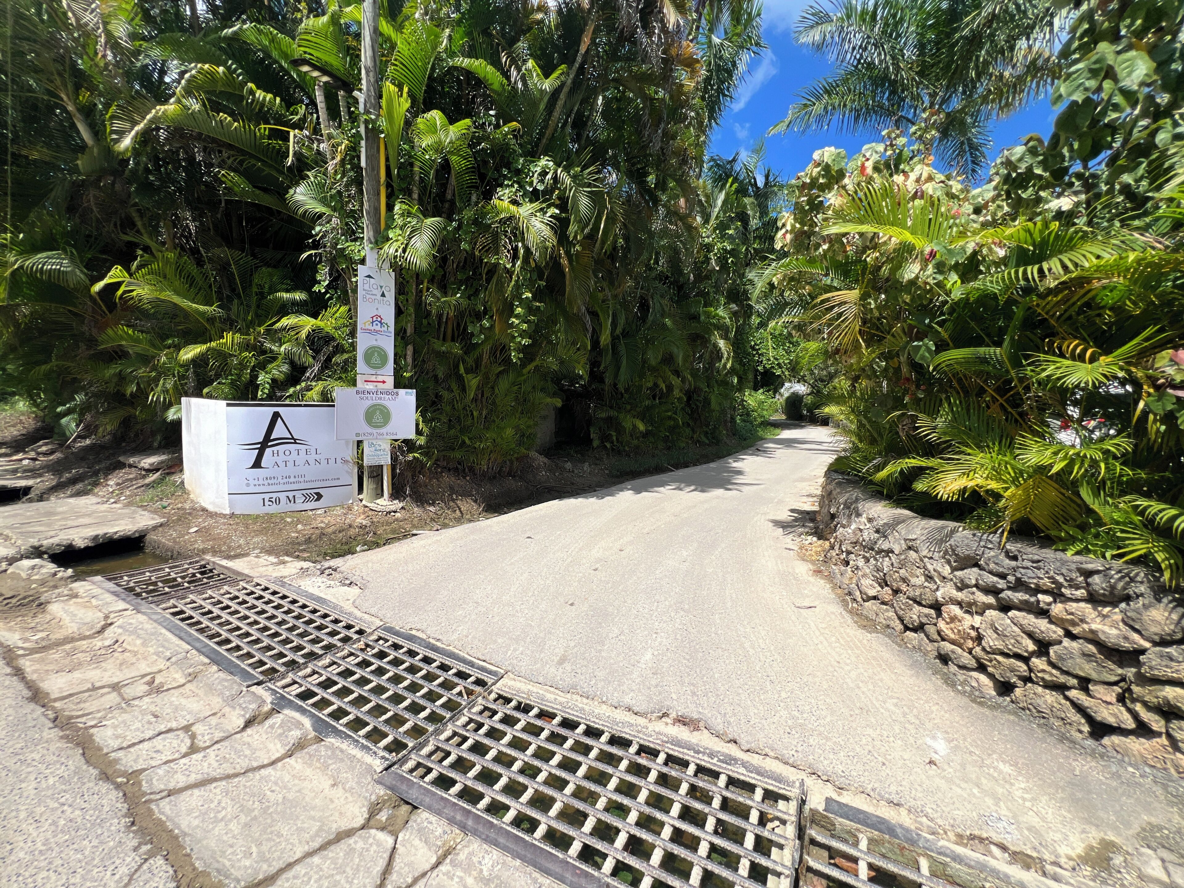 A tropical hotel entrance with a sign indicating amenities and a stone pathway.