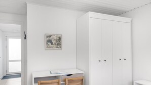 Una stanza con un'armadio bianco, una scrivania con due sedie di legno e un quadro appeso al muro.