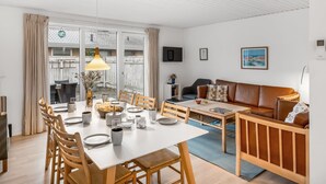 Zona pranzo con tavolo imbandito per quattro persone, un divano e una TV a parete.