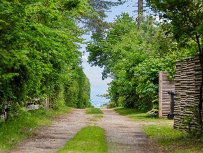 A gravel path leading to a stone wall with a wooden gate, surrounded by lush greenery and a view of the sea. - "Hoat" - 250m from the sea by Interhome (Gilleleje)