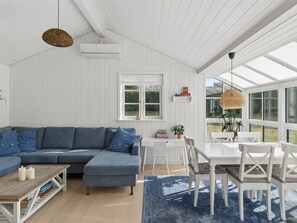 Ein modernes Wohnzimmer mit einer Eckcouch, einem Esstisch mit Stühlen, einem großen Fenster und einem Deckenventilator.
