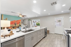 A modern kitchen with a large island, white cabinetry, a ceiling fan, and a window with a view of greenery. - Desert Diamond - Scottsdale 4 BR, Pool, Fire Pit, Ping Pong and games (Scottsdale)
