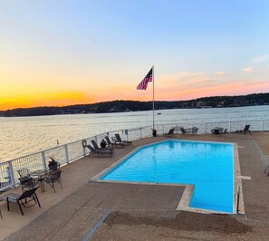 Ein Swimmingpool mit Liegestühlen und einer Flagge mit Blick auf ein Gewässer im Sonnenuntergang.