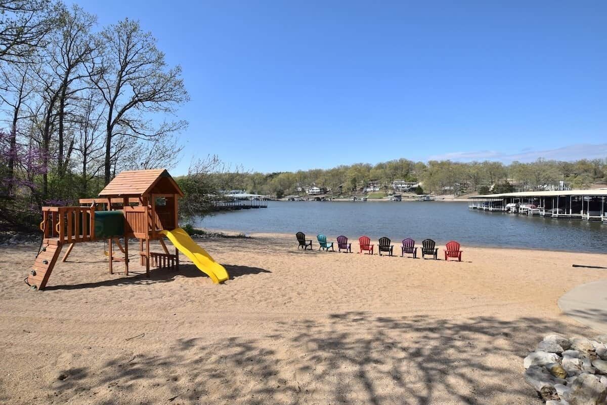 Ein Sandstrand mit einer hölzernen Spielanlage und einer Reihe Adirondack-Stühle.