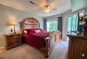 A bedroom with a wooden bed, a nightstand, a dresser, a ceiling fan, and a window with curtains.