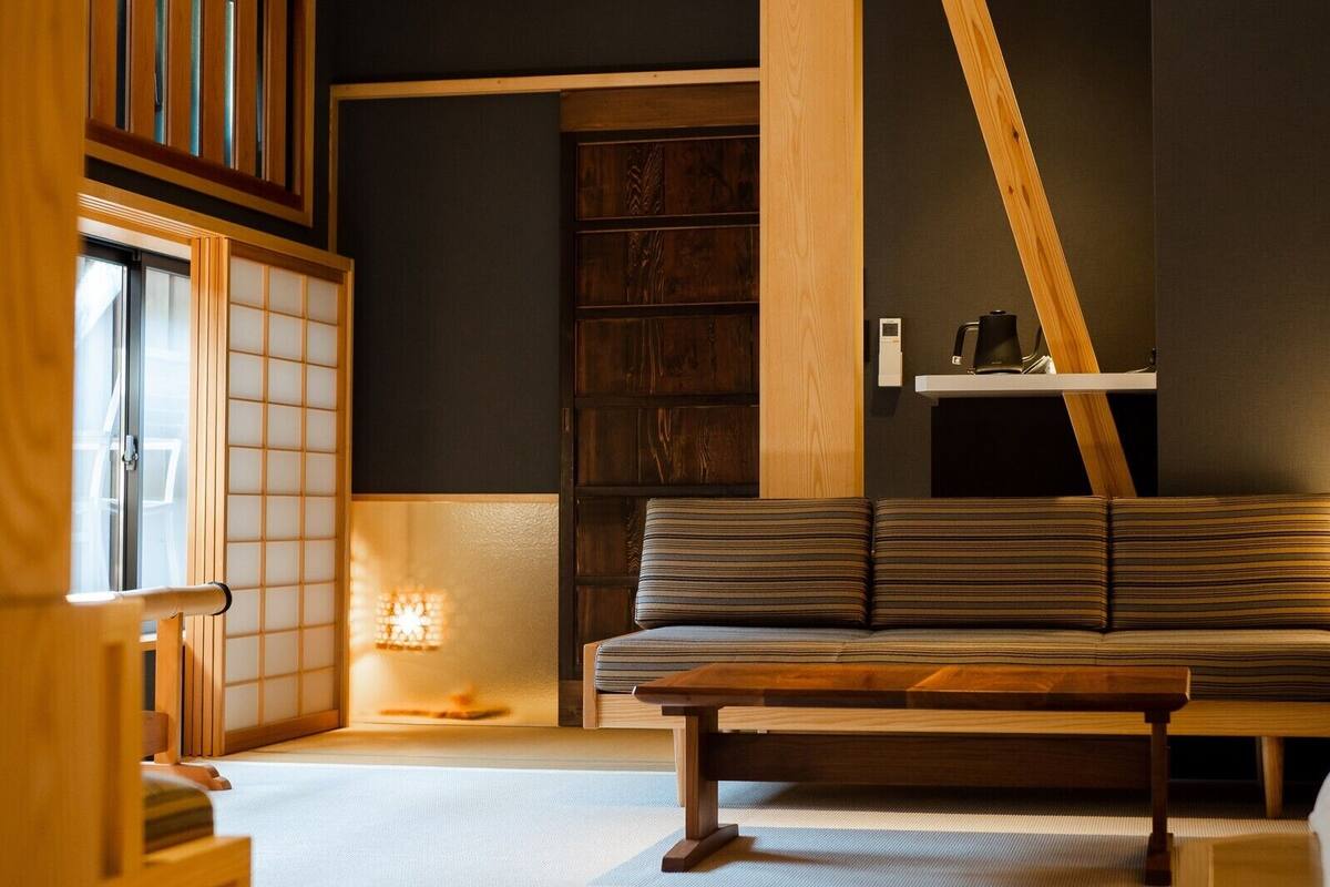 Una habitación tradicional japonesa con suelo de tatami, una mesa de madera baja, un sofá y una puerta corredera shoji.