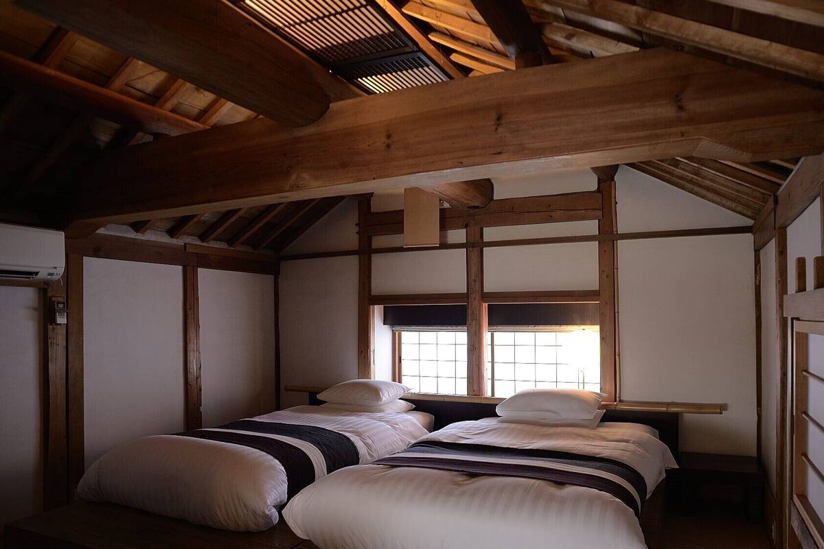 Una habitación tradicional japonesa con suelo de tatami, techo bajo con vigas de madera, una puerta corredera y una ventana con vistas.