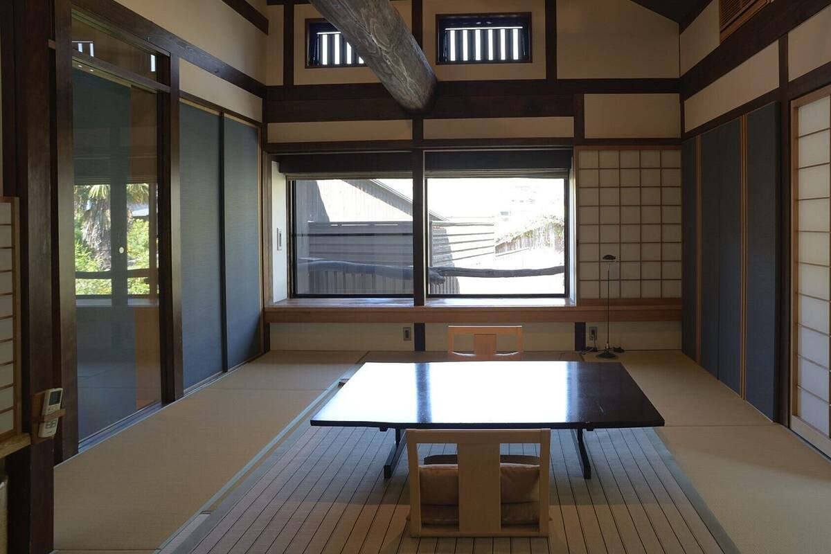 Una habitación japonesa tradicional con suelo de tatami, una mesa baja, puertas correderas y un ventanal grande.