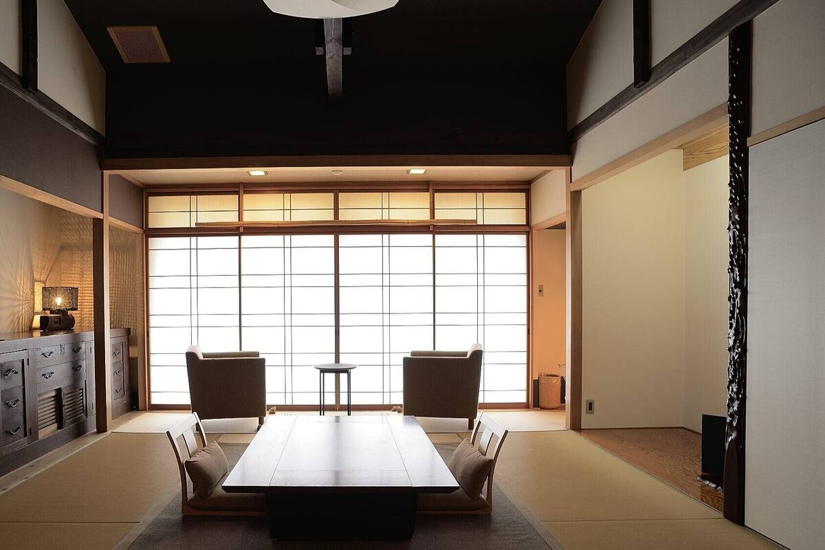 Una habitación japonesa tradicional con suelo de tatami, una mesa baja, dos sillas, un armario y un amplio puertas correderas shoji.