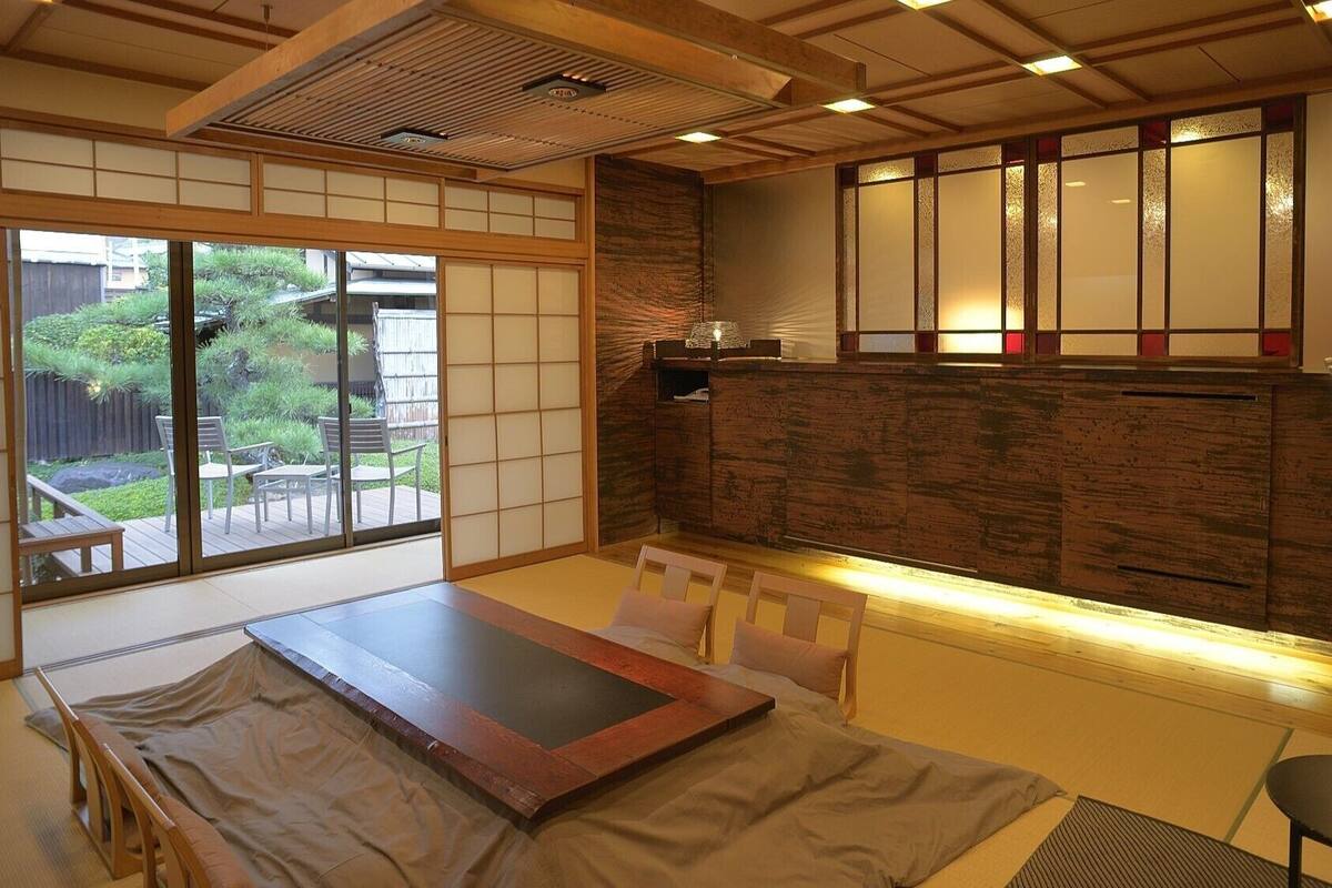 Una habitación de estilo japonés tradicional con suelo de tatami, una mesa de madera baja, puertas correderas y vistas a un jardín.
