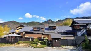 A row of traditional Japanese-style houses with sloped roofs, surrounded by a landscaped garden and a mountainous backdrop. - Shimayado Mari (Shodoshima)