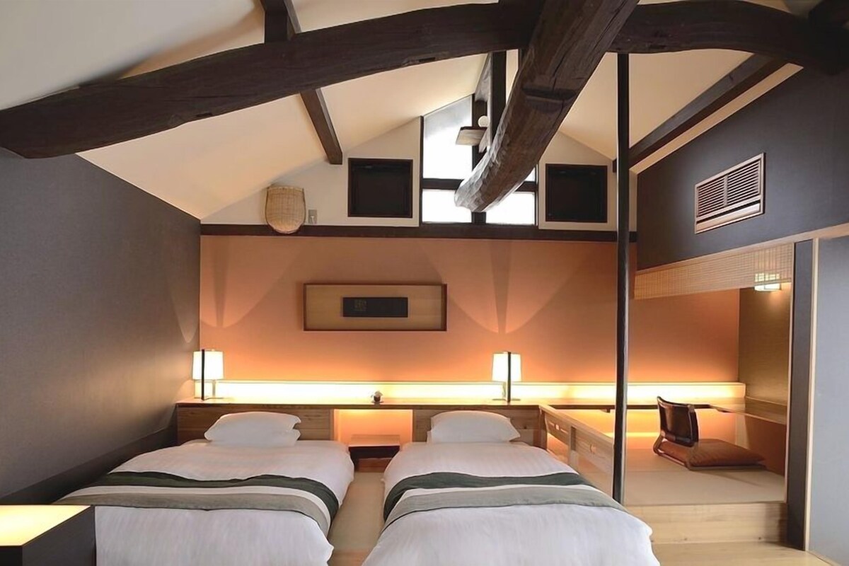 A hotel room with two beds, a large window, and a view of the sky.