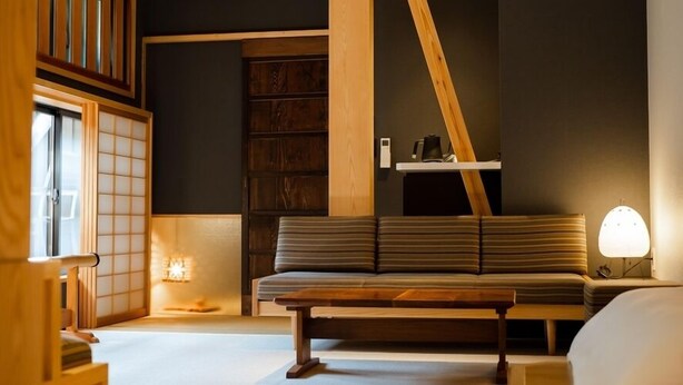 A modern interior with a sofa, a wooden shelf, and a traditional Japanese sliding door. - Shimayado Mari (Shodoshima)