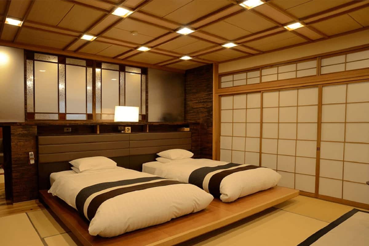 Un dormitorio tradicional japonés con dos camas, techo de madera y puertas correderas shoji.