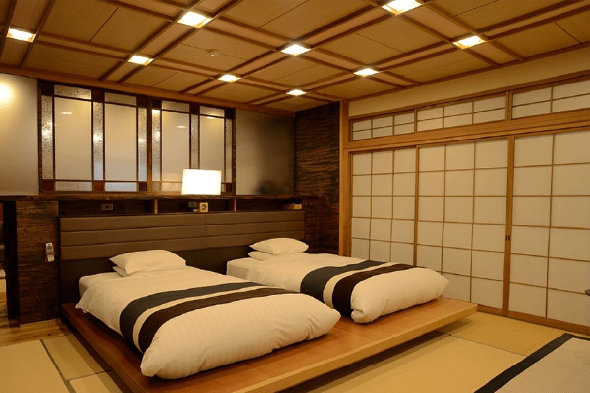 A traditional Japanese-style bedroom with two beds, a wooden ceiling, and sliding shoji doors.