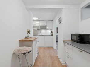 Eine kleine Küche mit weißen Schränken, einer Holz Arbeitsplatte, einem Barhocker und einer Mikrowelle.