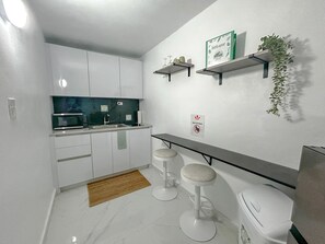 A compact kitchen with white cabinets, a microwave, a sink, and a small bar area with stools. - Anvil Forest Escape III|2 PPL|POOL|Generator|PKG| 15min Beach (Río Grande)