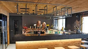 A bar area with wooden ceiling, bar stools, and a counter with a bartender.