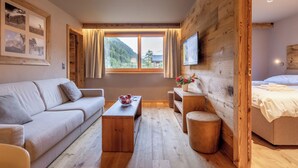 A modern room with a sofa, a wooden coffee table, a small round ottoman, a bed, and a TV mounted on the wall.