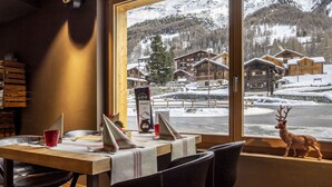 A dining area with a table set for two, a wooden bench, and a view of a snowy mountain landscape through a large window.