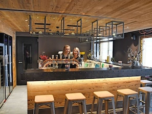 Eine Bar mit Holzbalkendecke, Barhocker und einer Theke mit Barkeeper.