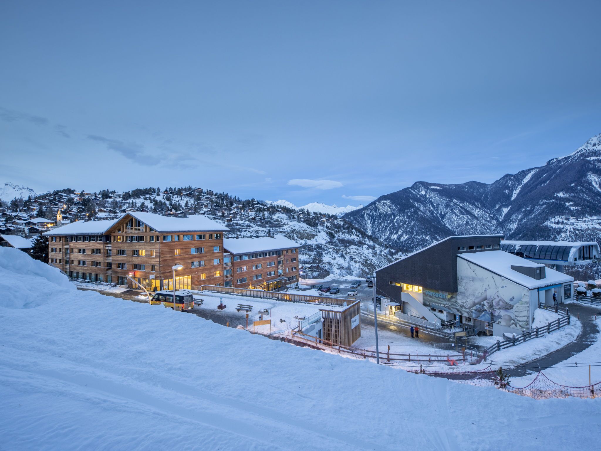 Ein Hotel mit mehreren Etagen, einer Seilbahn und schneebedeckten Bergen im Hintergrund.