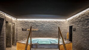 A spa area with a hot tub, stone walls, and wooden steps leading to it.