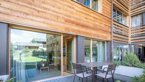 A modern building with a wooden exterior, large glass doors, and a deck with outdoor furniture.