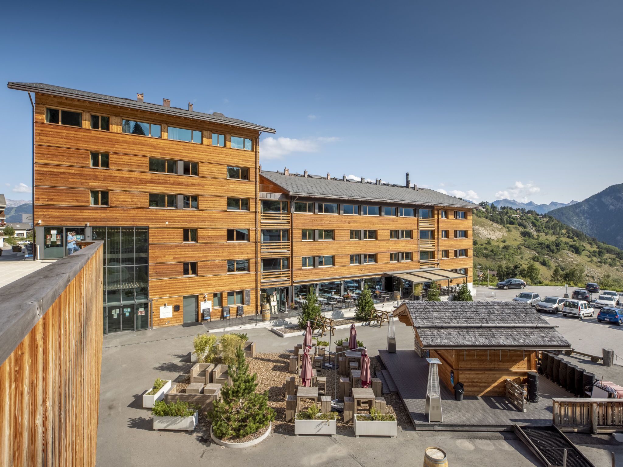 A multi-story wooden building with a covered outdoor seating area and a parking lot.