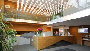 Un comptoir d’accueil moderne avec un revêtement en bois, une rambarde en verre et un luminaire suspendu.