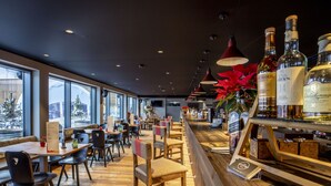 Un restaurant doté d’un bar, de tables et de chaises en bois, ainsi que de grandes fenêtres.